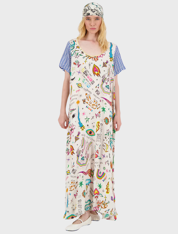 A woman in a vibrant, patterned dress stands confidently, showcasing colorful designs that reflect her unique style.