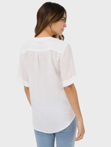 A white linen blouse by Veri, illustrating its minimalist design and lightweight material, displayed on a hanger.
