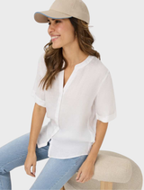 A white linen blouse by Veri, featuring a simple yet stylish design, hanging against a neutral background.