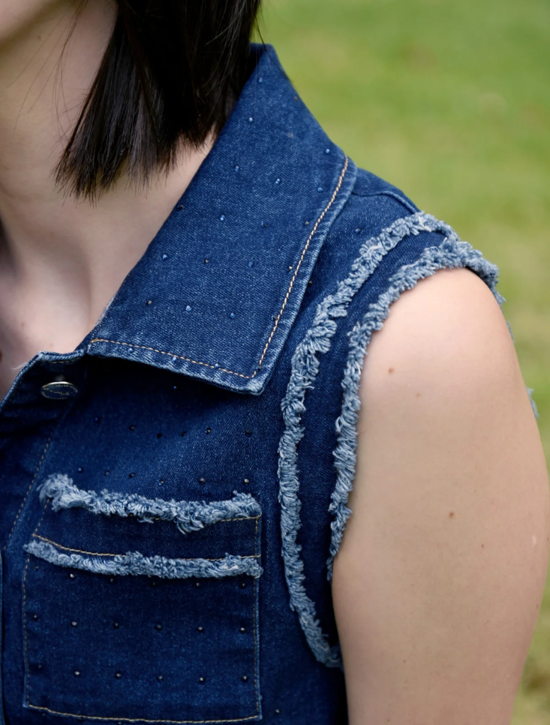 A woman sporting a denim vest and jeans stands, representing a laid-back and chic fashion choice.