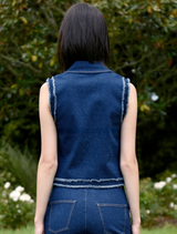 A woman in a denim vest and jeans smiles, embodying a casual and trendy style.