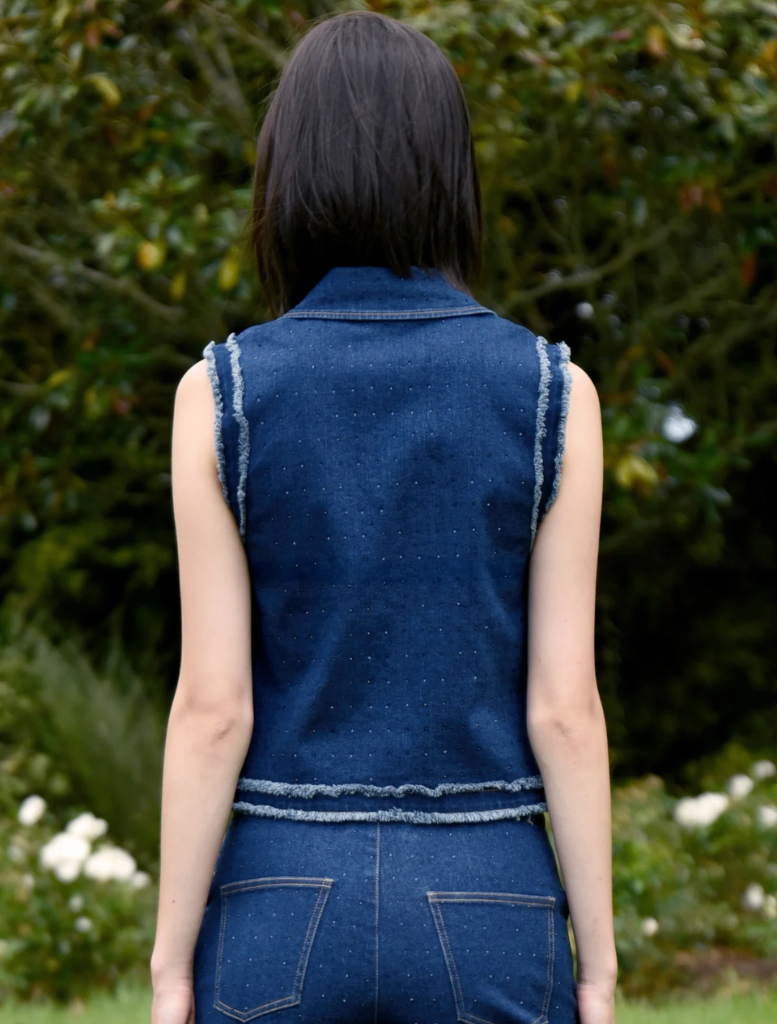 A woman in a denim vest and jeans smiles, embodying a casual and trendy style.