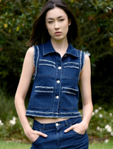 A woman wearing a denim vest and jeans stands confidently, showcasing a casual and stylish outfit.