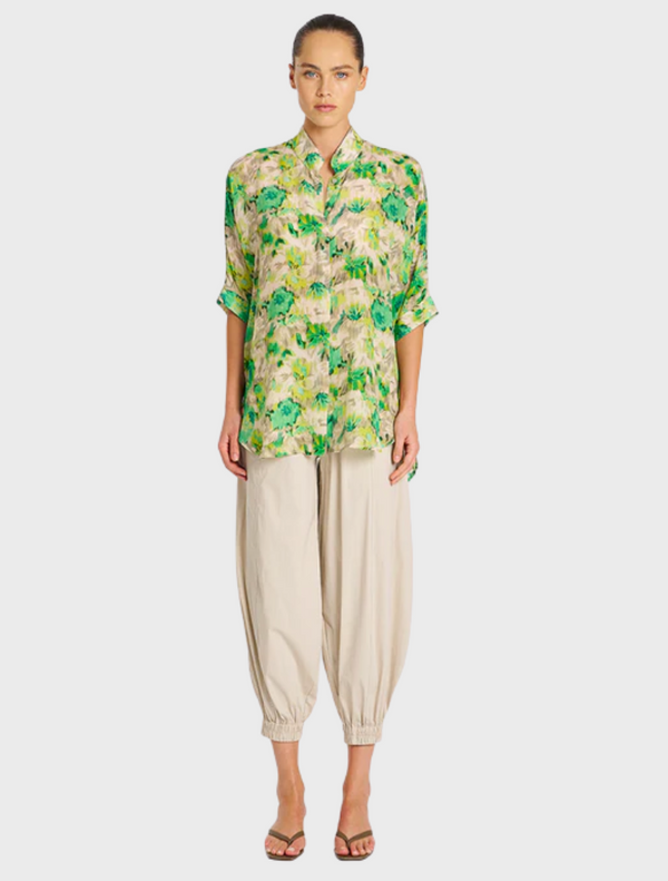 A model showcases a green and yellow floral shirt, featuring vibrant patterns and a relaxed fit.