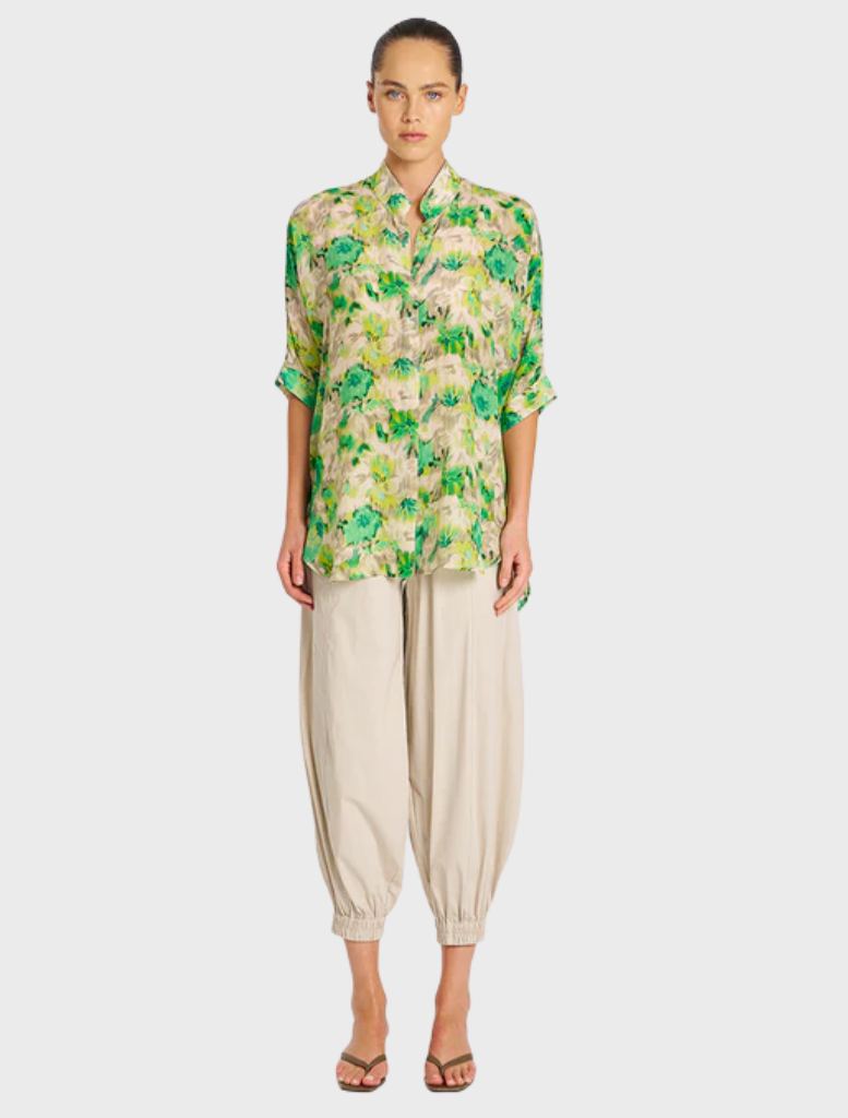 A model showcases a green and yellow floral shirt, featuring vibrant patterns and a relaxed fit.