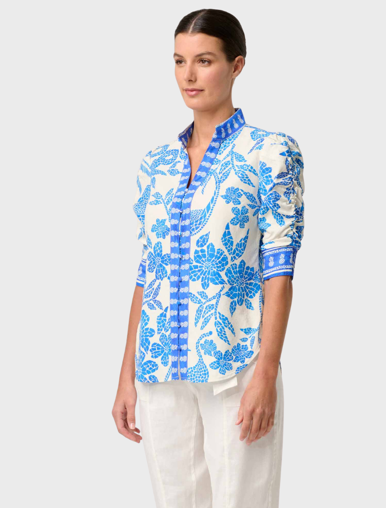 A woman models a blue and white Azure Mosaic shirt with rouched sleeves, showcasing the Calantha Viscose Dobby design.