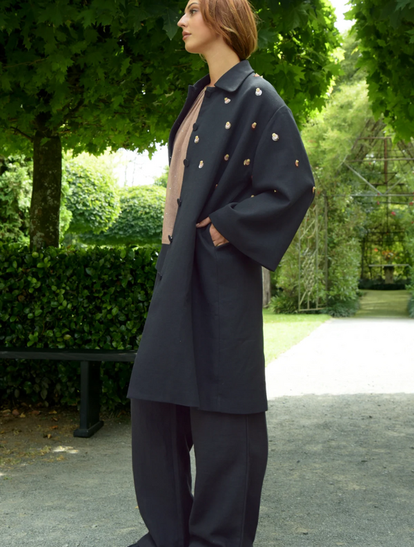A woman dressed in a black coat and black pants, exuding a chic and modern look.