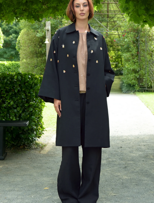 A woman wearing a black coat and black trousers, showcasing a stylish outfit.