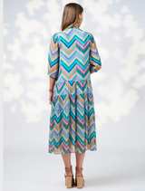 A woman dressed in a blue jacket and a colorful Wanderlust Midi Dress, showcasing a stylish outfit.