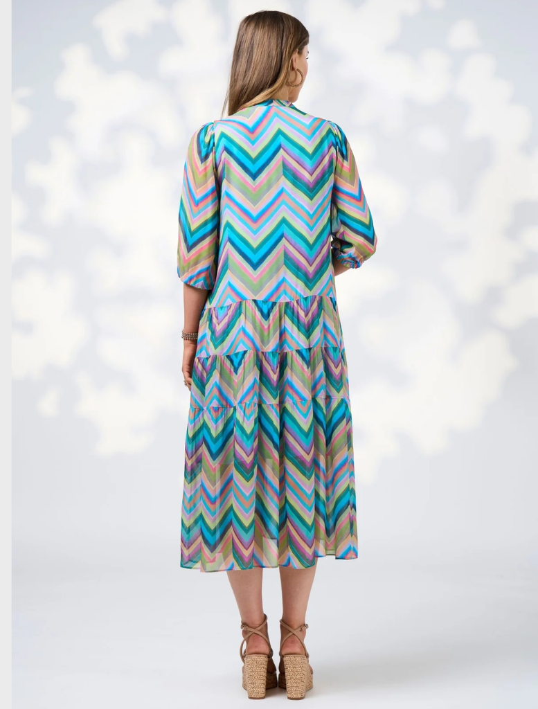 A woman dressed in a blue jacket and a colorful Wanderlust Midi Dress, showcasing a stylish outfit.