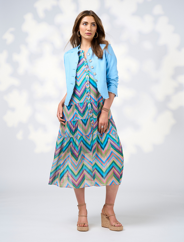 A woman wearing a blue jacket over a multi-colored Wanderlust Midi Dress.
