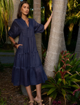 Tiered indigo ramie midi dress featuring a V-neck, gathered sleeves, raw bias trim, and hidden side seam pockets.