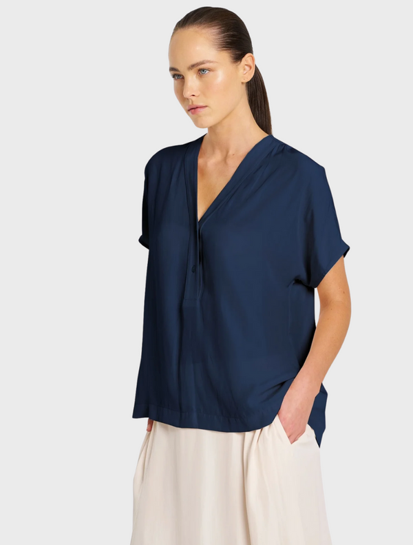 The model is dressed in a navy shirt and a white skirt, presenting a chic and fashionable look.
