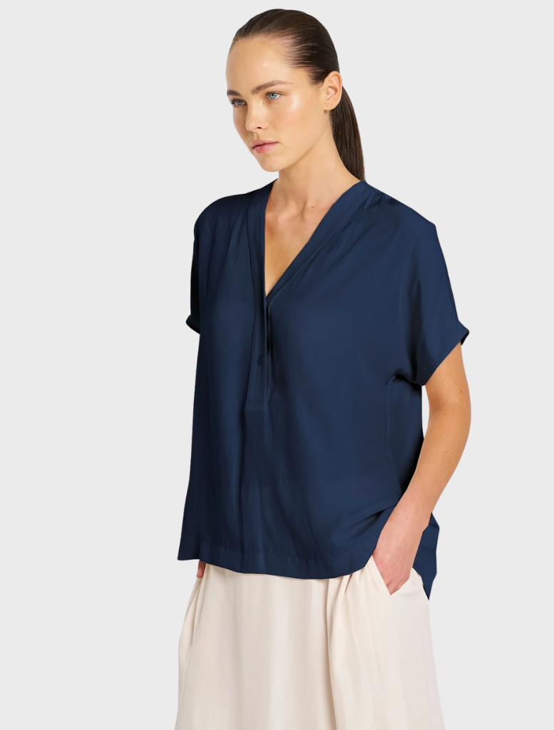 The model is dressed in a navy shirt and a white skirt, presenting a chic and fashionable look.