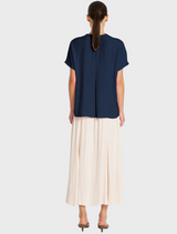The model wears a navy shirt along with a white skirt, exemplifying a trendy and sophisticated outfit choice.
