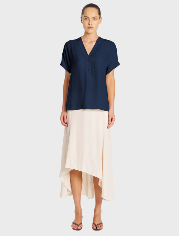 A model poses in a navy shirt paired with a white skirt, showcasing a stylish and modern outfit.