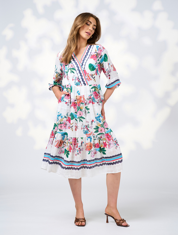 A model displays the Pandora Dress - White Multi, featuring a v-neck and a white floral pattern.