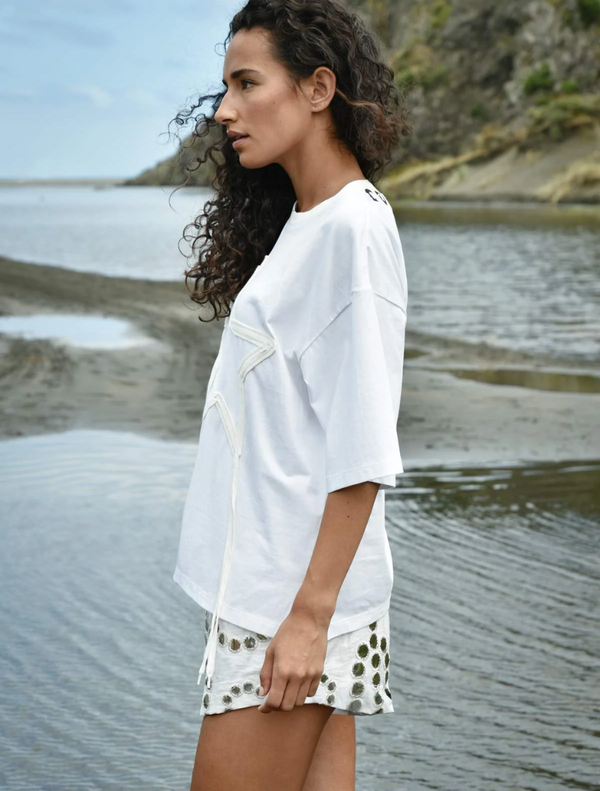 A woman wearing a white shirt and shorts stands near the water, enjoying the view of the calm surroundings.