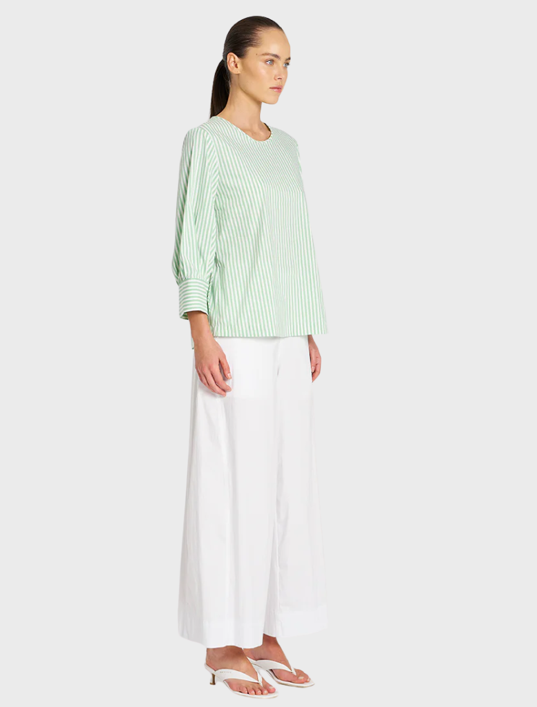 The model is dressed in a green top and white wide-legged pants, presenting a chic and contemporary fashion look.