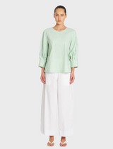 A model showcases a green top paired with white wide-legged pants, highlighting a stylish and modern outfit.