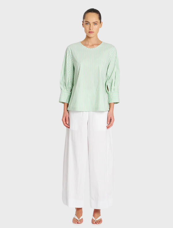 A model showcases a green top paired with white wide-legged pants, highlighting a stylish and modern outfit.