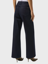 A woman in dark blue wide leg jeans, posing with a relaxed expression and hands on her hips.