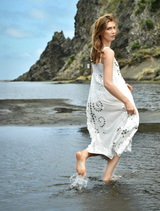 A woman in a white dress stands on the beach, surrounded by sand and water, enjoying the serene coastal view.