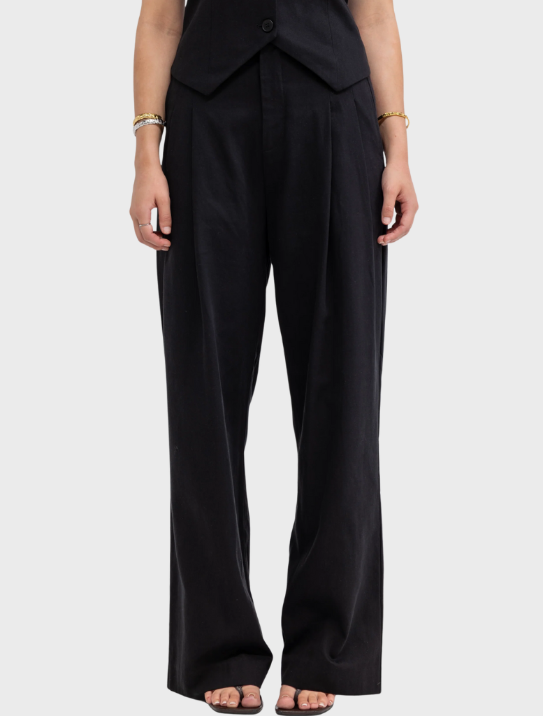 A woman dressed in black pants and a vest stands confidently, showcasing a stylish and professional appearance.