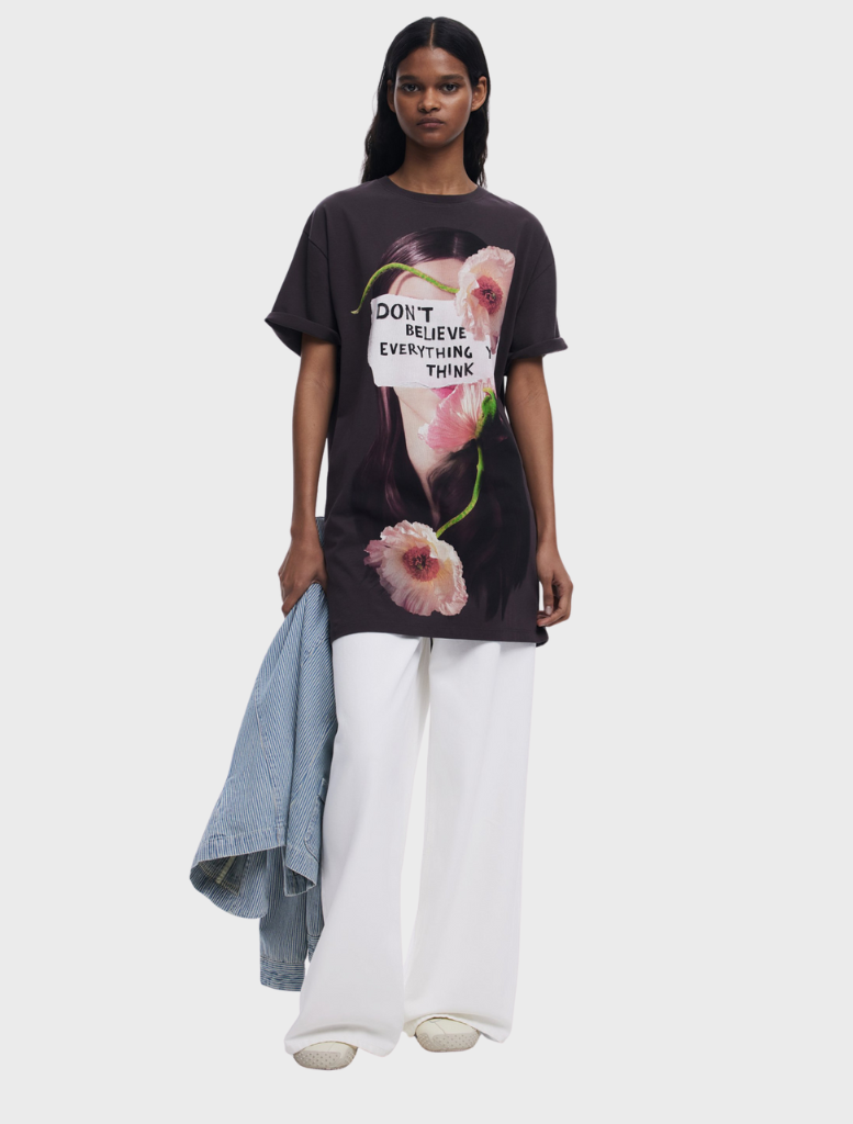 A woman displays a t-shirt with the words "don't live everything to," encouraging reflection on life choices.