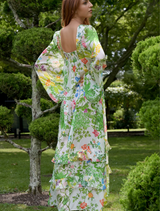 A woman in a colorful floral dress walks through a park, immersed in the beauty of nature.