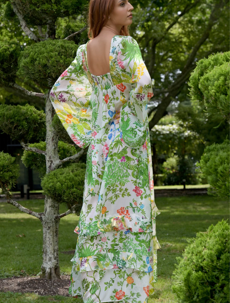 A woman in a colorful floral dress walks through a park, immersed in the beauty of nature.