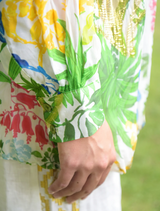 A woman Shirt in a floral pattern walks along a path in a park, with lush greenery surrounding her.