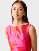 A woman wearing a pink and red dress stands gracefully, showcasing a vibrant and stylish outfit.