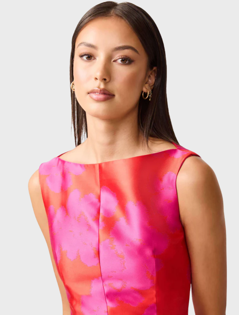 A woman wearing a pink and red dress stands gracefully, showcasing a vibrant and stylish outfit.