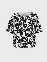 A black and white patterned top leans against a fence, her posture relaxed and inviting.