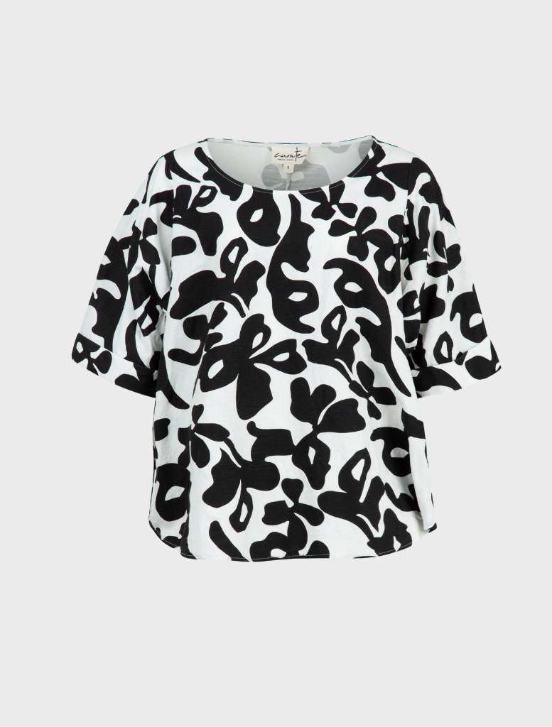 A black and white patterned top leans against a fence, her posture relaxed and inviting.
