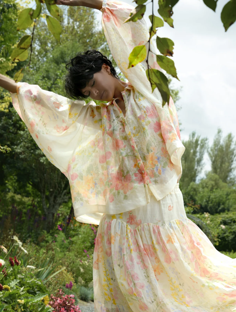 A woman in a colorful floral dress walks through a park, immersed in the beauty of nature.