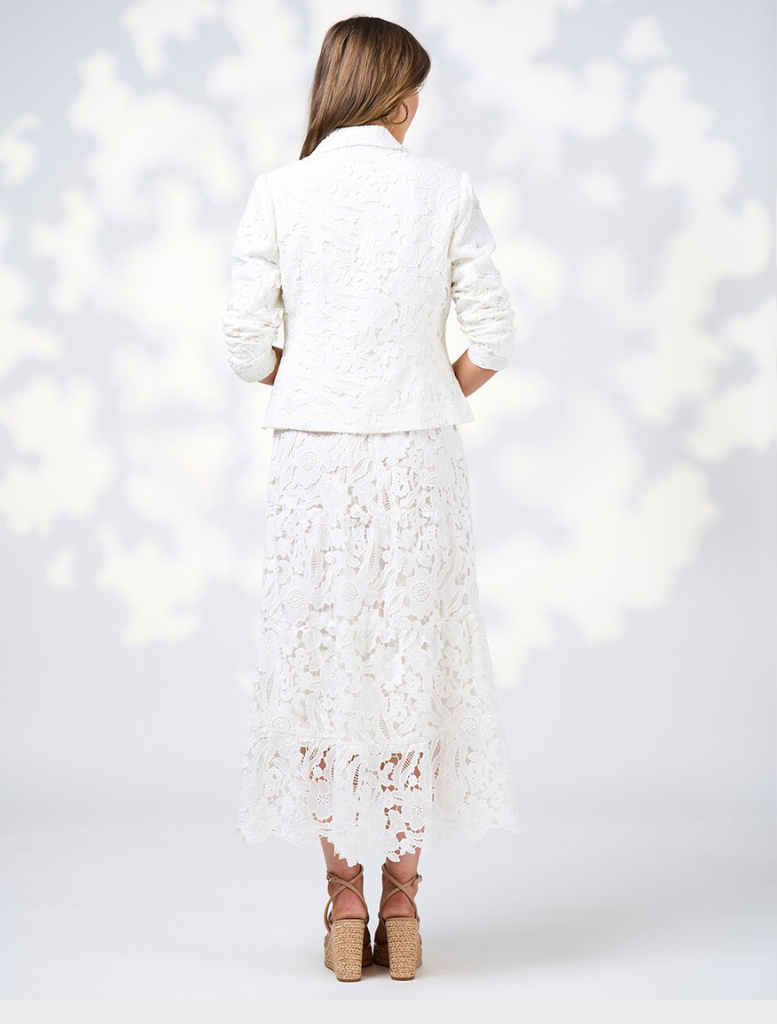  A woman dressed in a white silk jacket and pants poses elegantly, highlighting her fashionable ensemble.