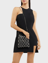 A woman in a black dress and heels strikes a pose on a street, featuring a black Kit Crystal Cage Bag.