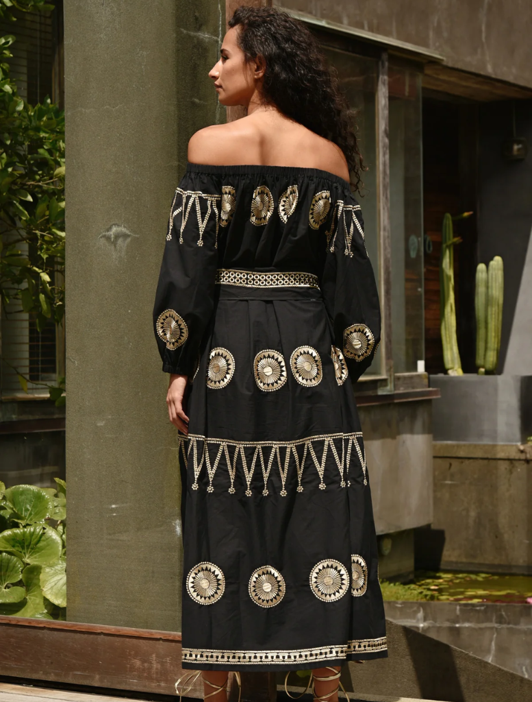 A woman in a black dress leans against a wall, presenting a graceful and composed figure.