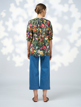 A model displays a floral blouse paired with wide-leg pants, highlighting the Looking Glass Top in Ivy Multi.