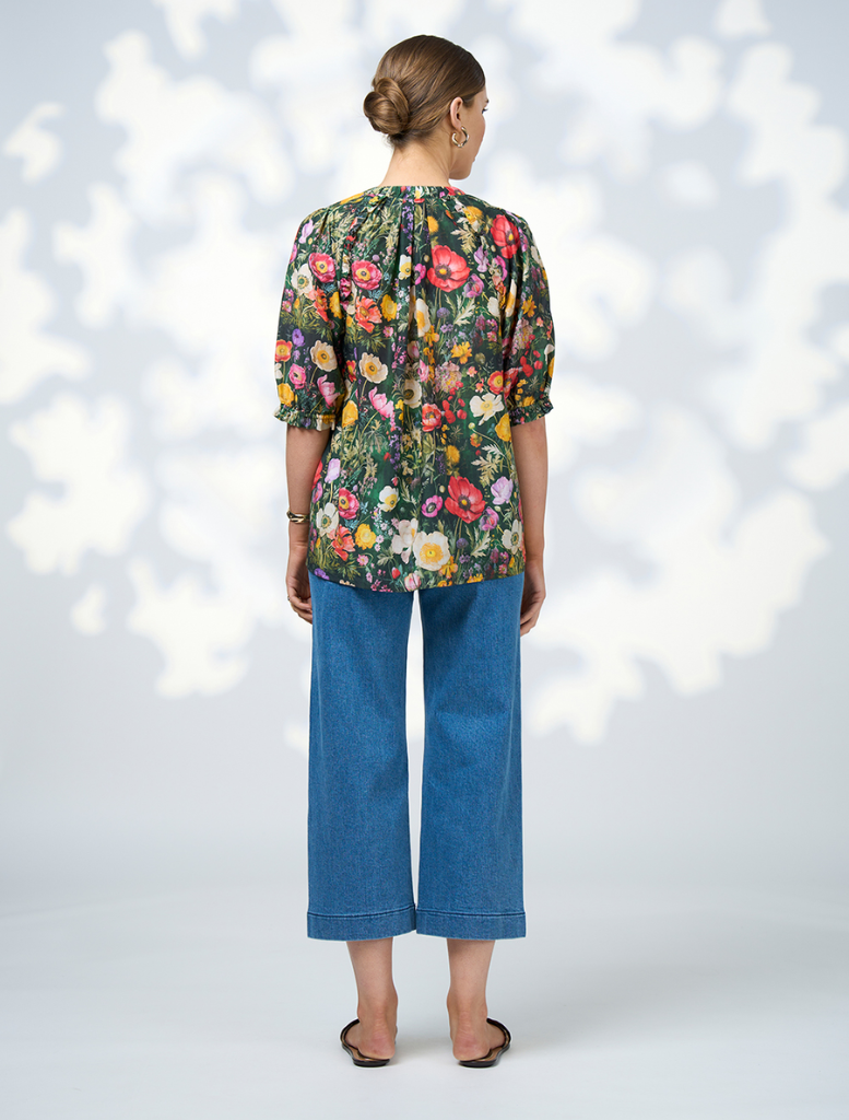 A model displays a floral blouse paired with wide-leg pants, highlighting the Looking Glass Top in Ivy Multi.