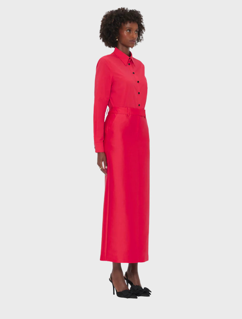  A woman wearing a red dress and black shoes stands confidently, showcasing her stylish outfit.