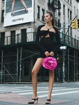A woman dressed in black holds a pink satin Rosita Rosette Frame Bag, emphasizing her chic fashion sense.

