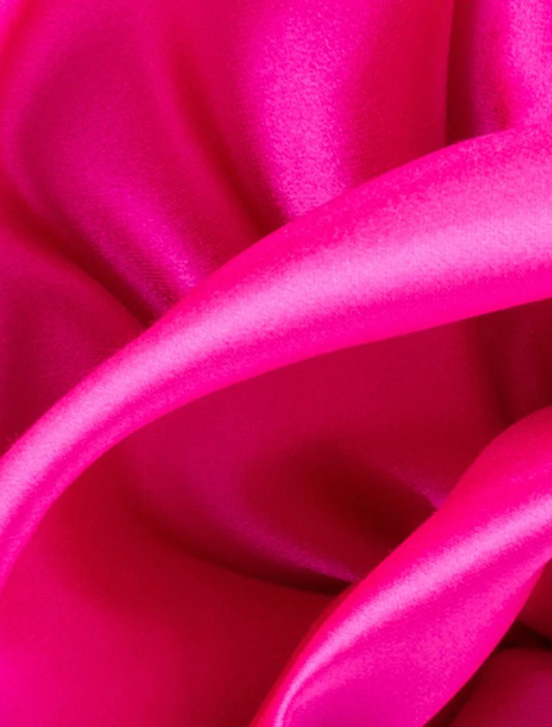 A pink satin flower bag, the Rosita Rosette Frame Bag in fuchsia, hanging from a chic chain.