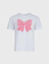  A white t-shirt with a bow smiles, captured in a lively outdoor environment.