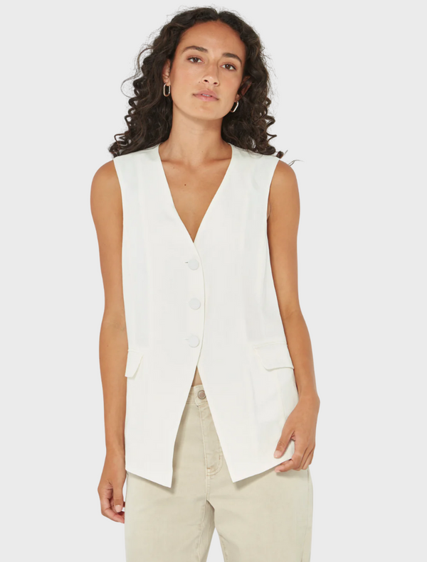 Front view of woman wearing a white button-front sleeveless vest with beige pants from Mariko Boutique