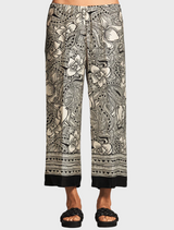 A woman models a floral print pant, showcasing vibrant colors and a stylish design.