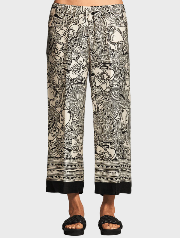 A woman models a floral print pant, showcasing vibrant colors and a stylish design.