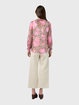 The Yala Blouse showcases a bold leopard and floral print, ruffle trim, button closure, and elastic cuffs, paired with a cami.